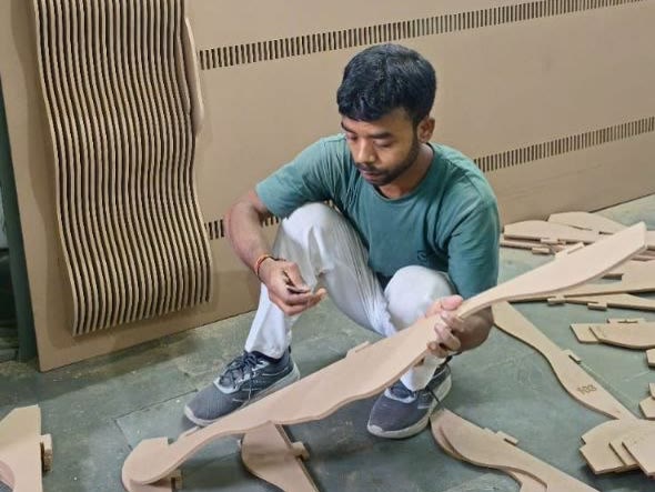 Dream3 fabricator checking a CNC cut rib profile against numbered parametric wall panel pieces laid out on the workshop floor in Bijwasan