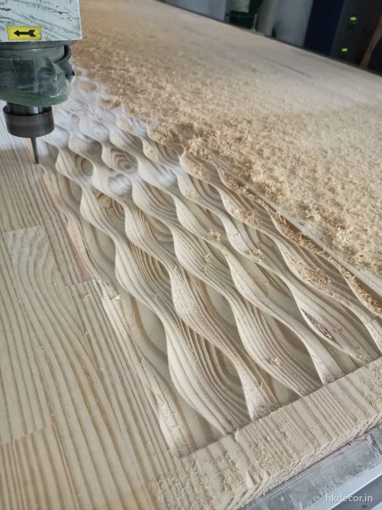 CNC router cutting a deep three-dimensional wave into raw board with depth varying across the surface